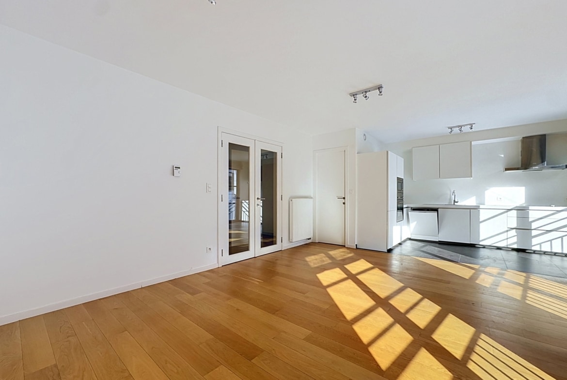 Licht appartement met open woonkamer, moderne witte keuken en parketvloer.