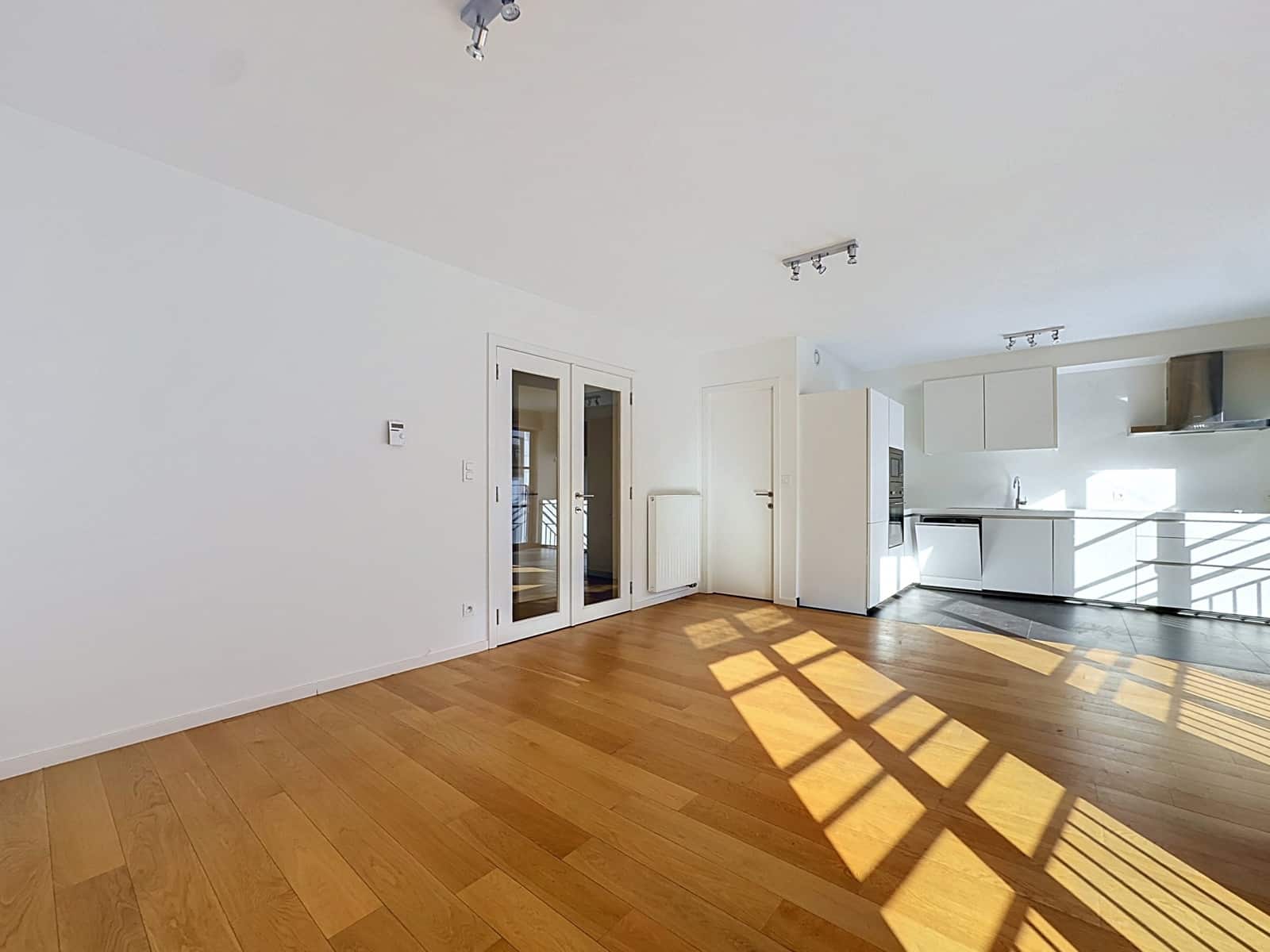 Open woonkamer met moderne keuken – You Real Estate Agency Licht appartement met open woonkamer, moderne witte keuken en parketvloer.