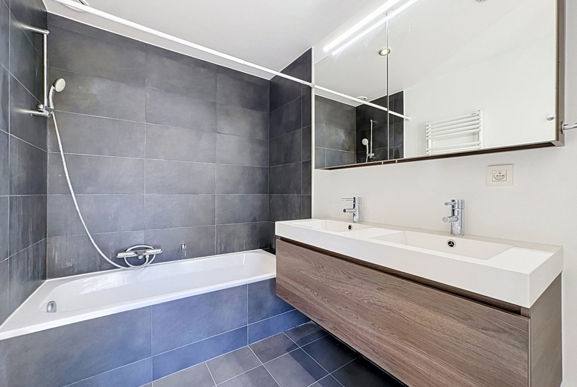 Moderne badkamer in een appartement met ligbad, dubbele wastafel en houten badkamermeubel.