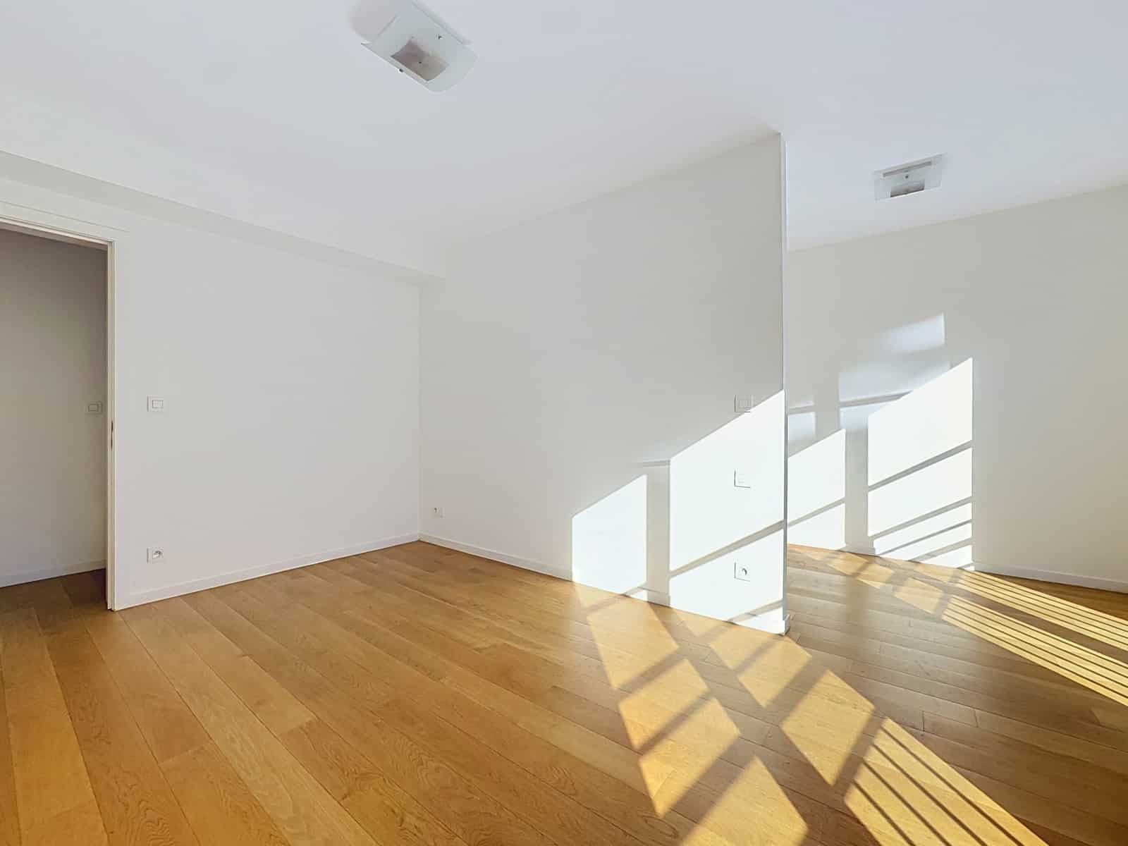 Lichte woonkamer met parketvloer - You Real Estate Agency Lichte, lege woonkamer met houten parketvloer in een modern appartement.