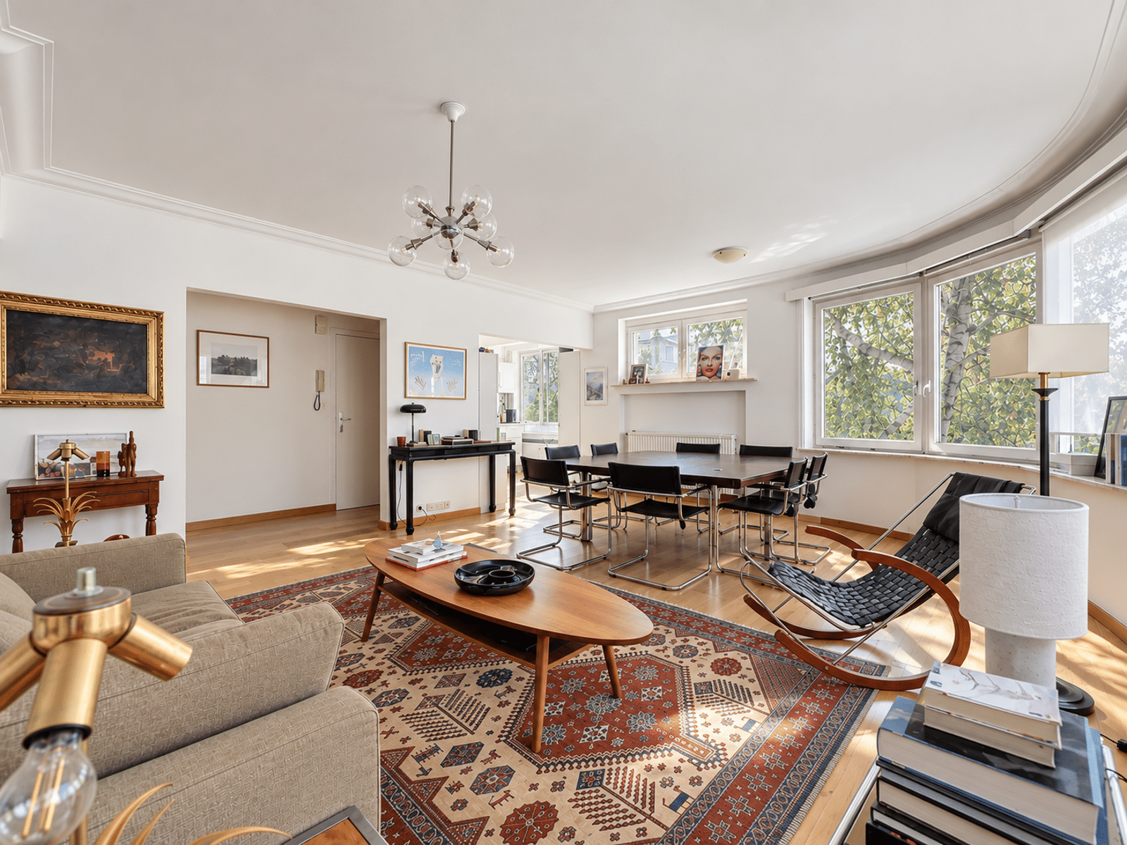 whise photo 5 Bright, open living and dining room with a wooden dining table and black chairs by large windows letting in sunlight.