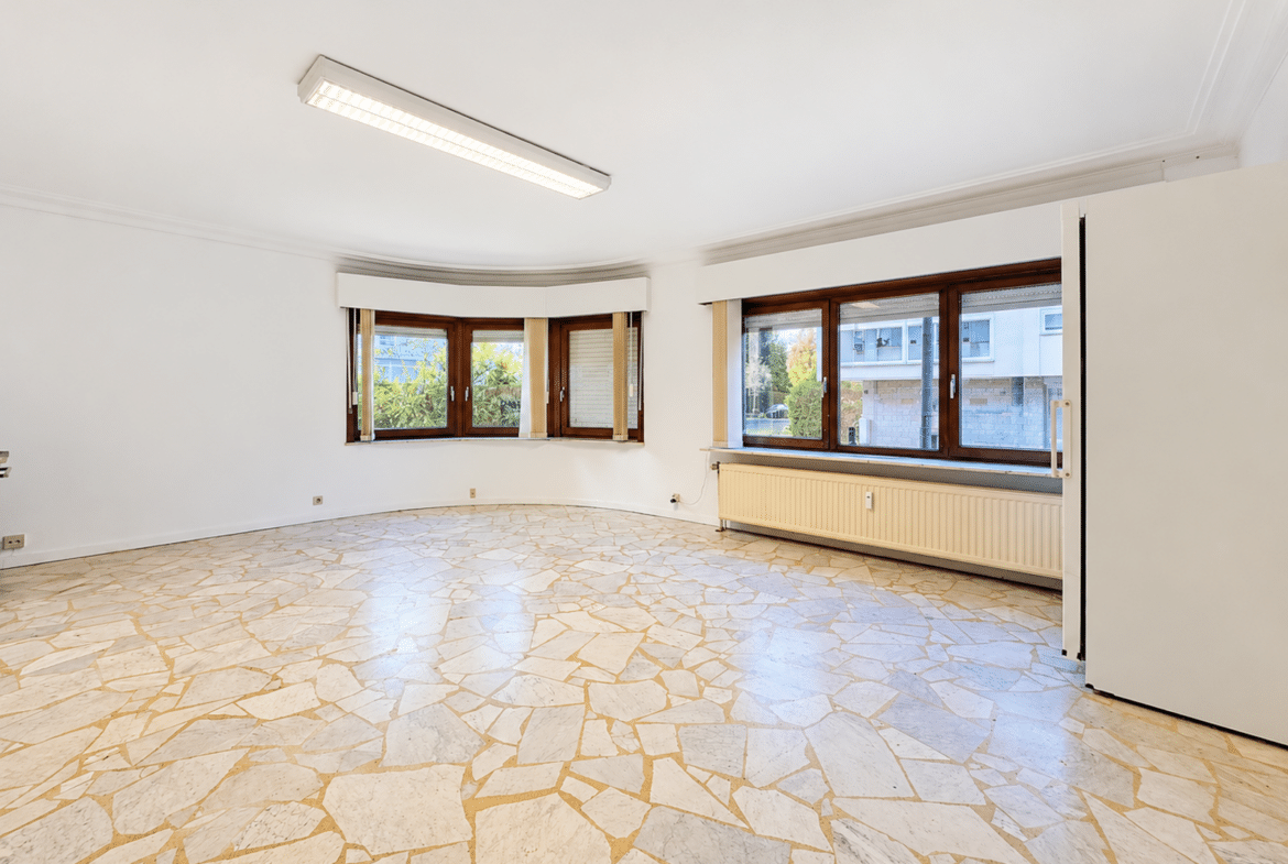 Bright empty living room with curved bay windows and a beige mosaic tile floor, white walls.