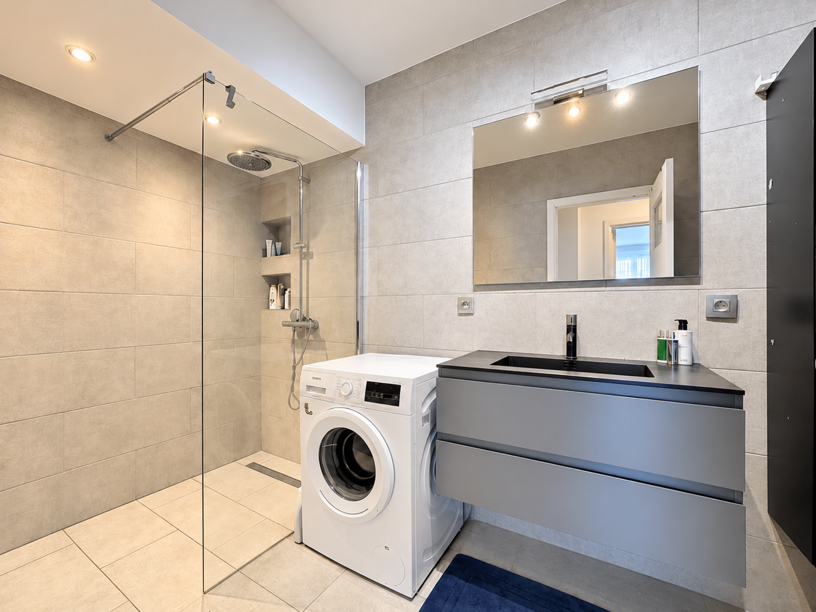 whise photo 13 Modern bathroom with glass shower enclosure to the left, rainfall showerhead, and built-in shelves; washing machine beside a gray vanity and large mirror.
