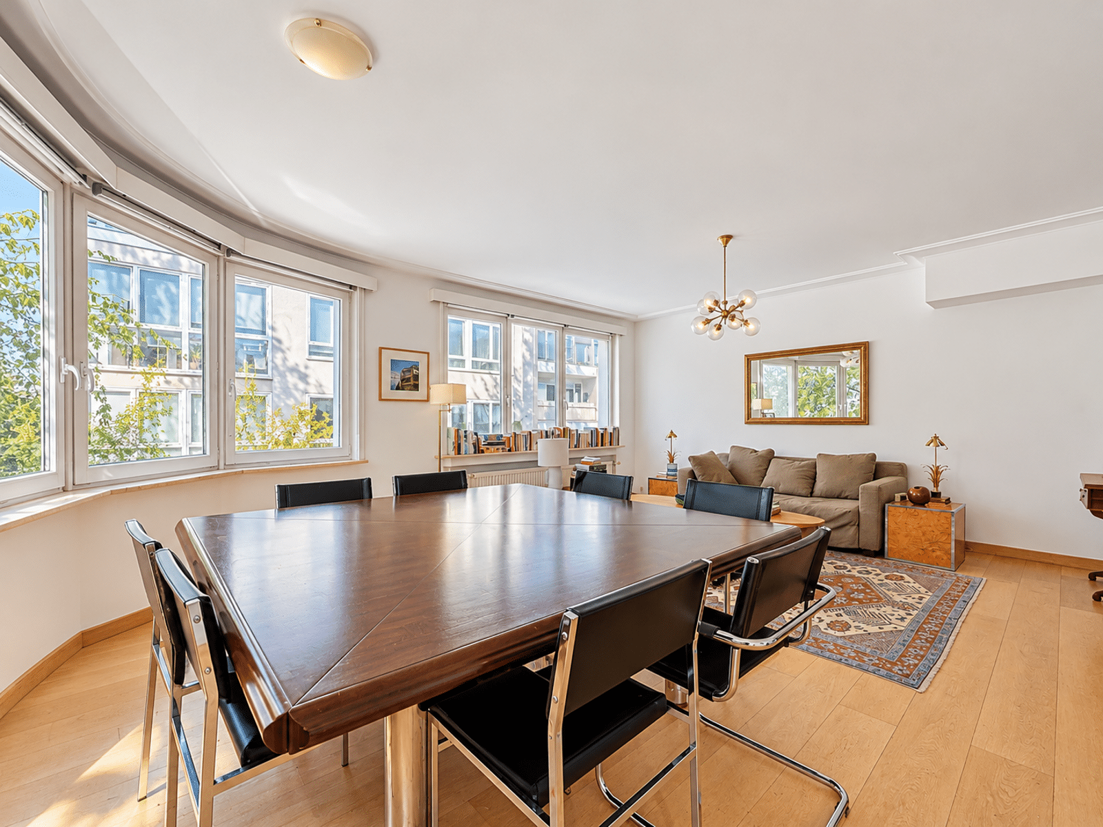 whise photo 3 Bright dining room with a long wooden table and black leather chairs, curved bay windows, and a seating area with a sofa.