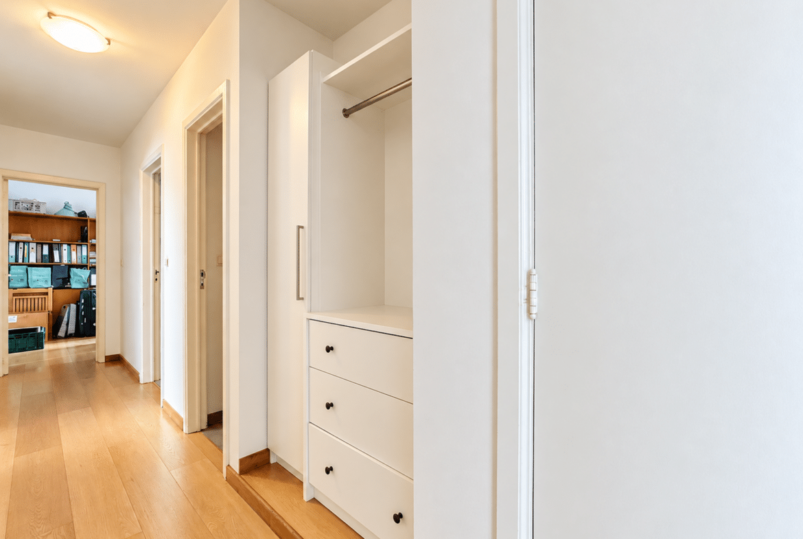 Bright hallway with white built-in wardrobe, open closet, and doors along a wooden floor.