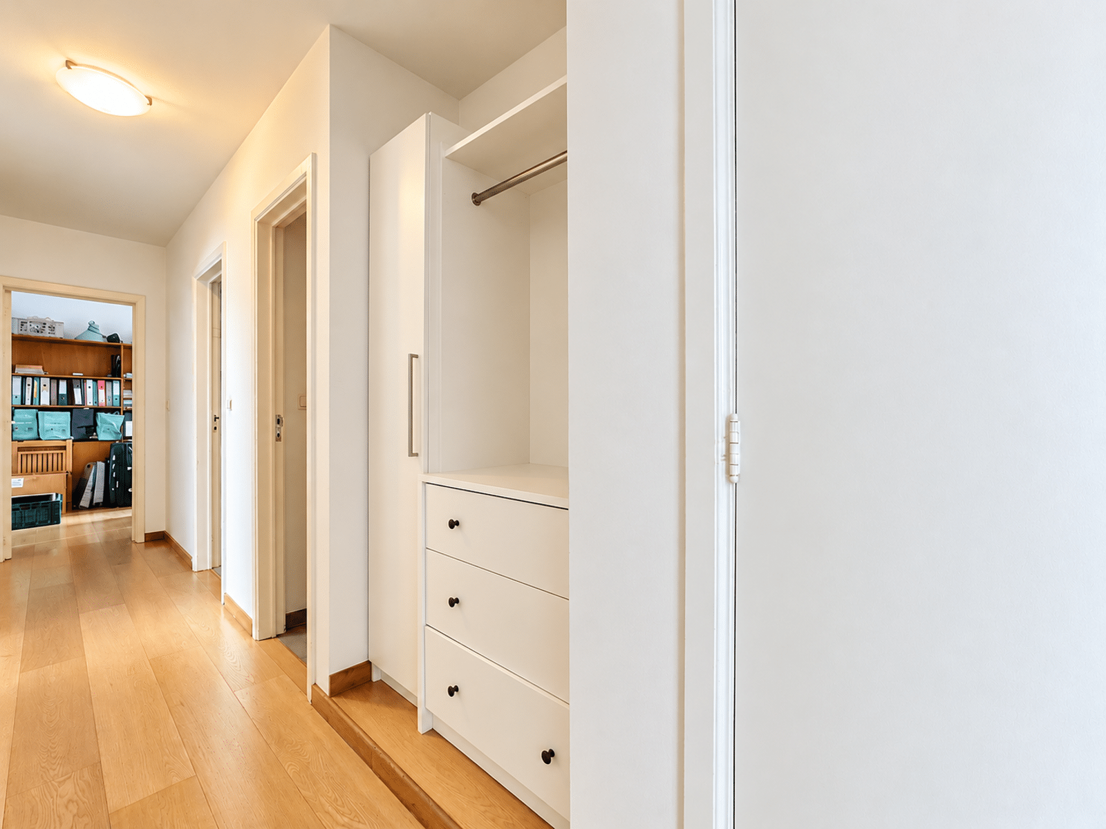 whise photo 14 Bright hallway with white built-in wardrobe, open closet, and doors along a wooden floor.