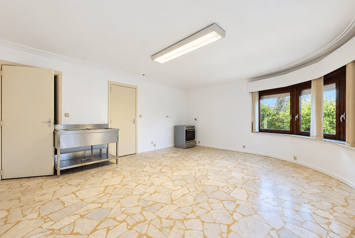 Grande pièce lumineuse avec coin cuisine et baie vitrée dans appartement à rénover.