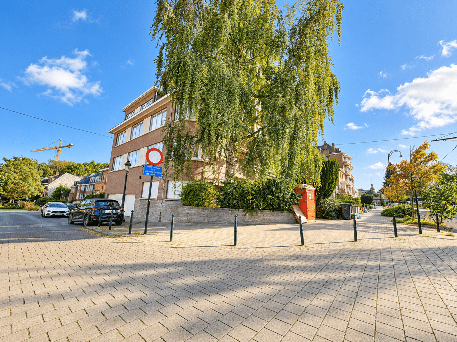 Vue Extérieure d’Immeuble Arboré – You Real Estate Agency Immeuble d’appartements en briques dans quartier résidentiel arboré.