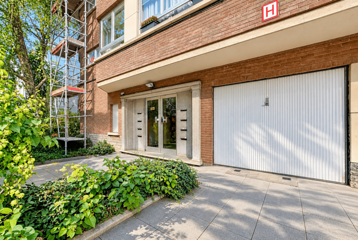 Façade d’immeuble résidentiel avec entrée, garage et échafaudage.