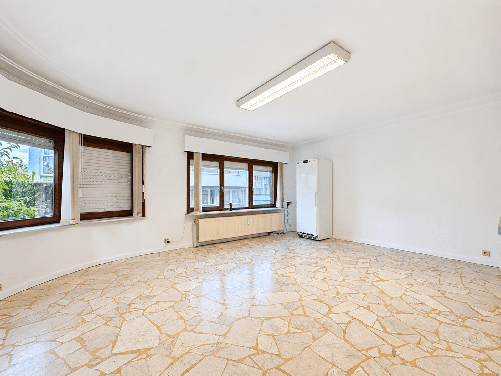 whise photo 17 Bright empty room with curved wall, three large brown-framed windows, a radiator beneath, and a tall white cabinet on the right.