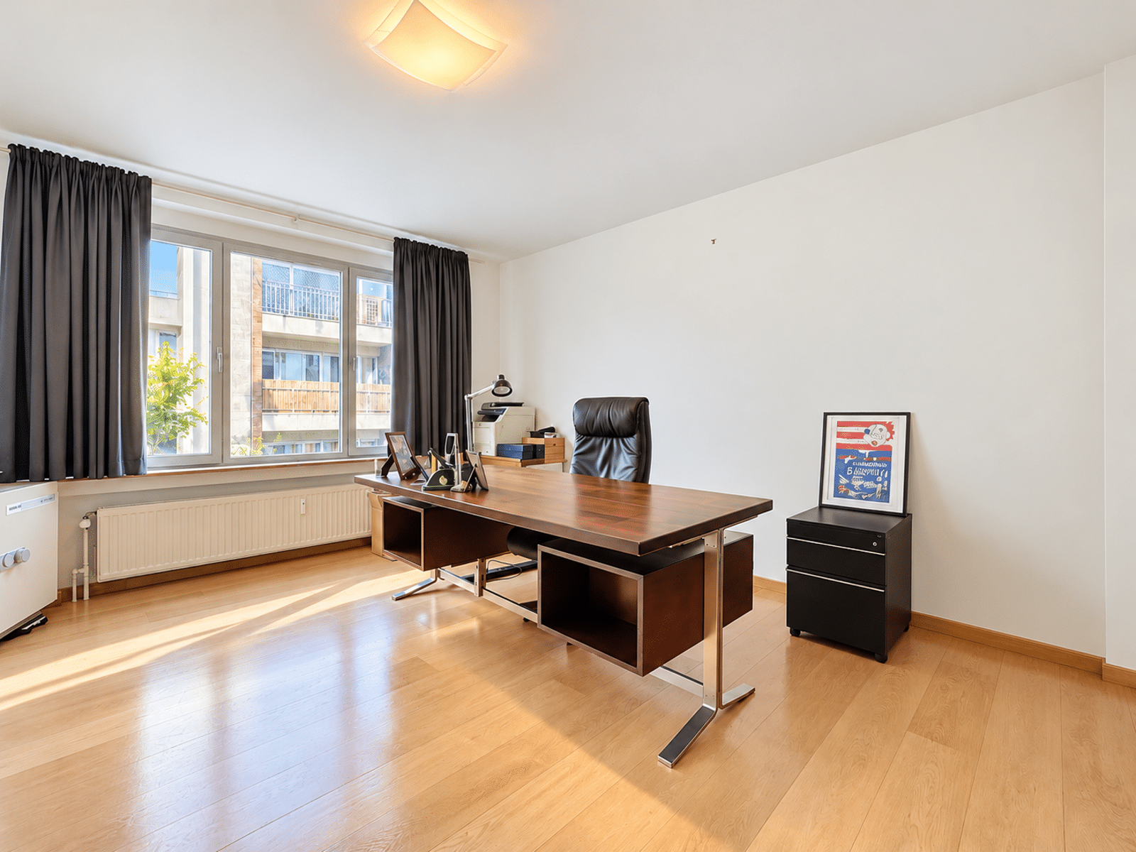 whise photo 11 Modern home office with a wooden desk, black leather chair, large window with dark curtains, and a framed poster on a small black cabinet.
