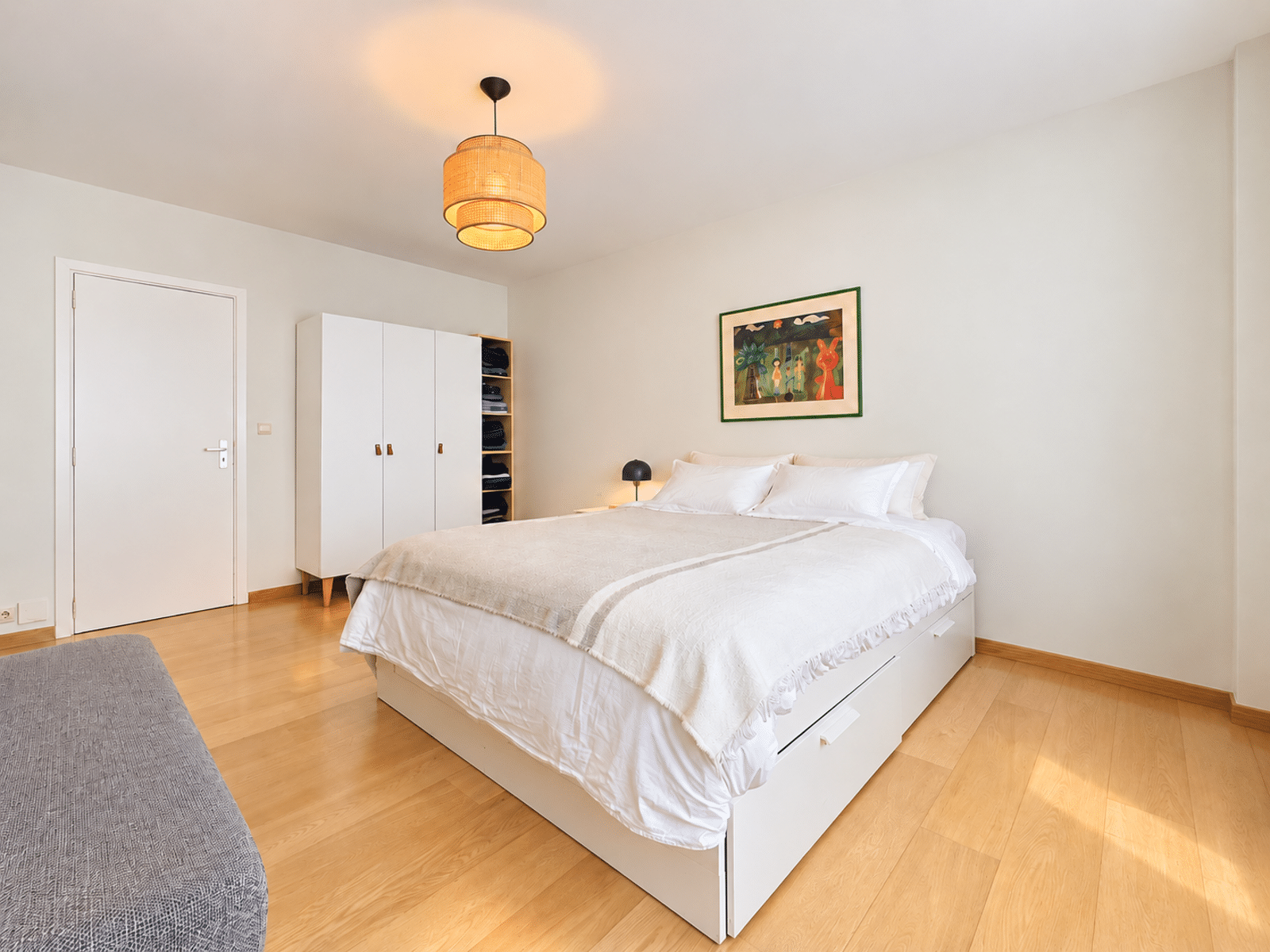 whise photo 9 Bright minimalist bedroom with a white bed, white wardrobe, and wooden floor; woven pendant light overhead.