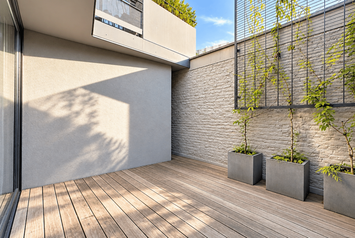 Terrasse moderne en bois avec treillis végétalisé et baie vitrée d’appartement.