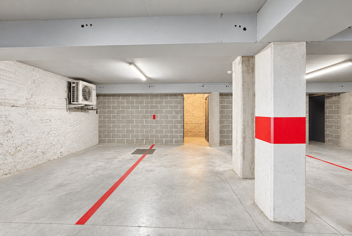 Parking intérieur sécurisé avec marquages rouges et colonnes en béton dans immeuble moderne.