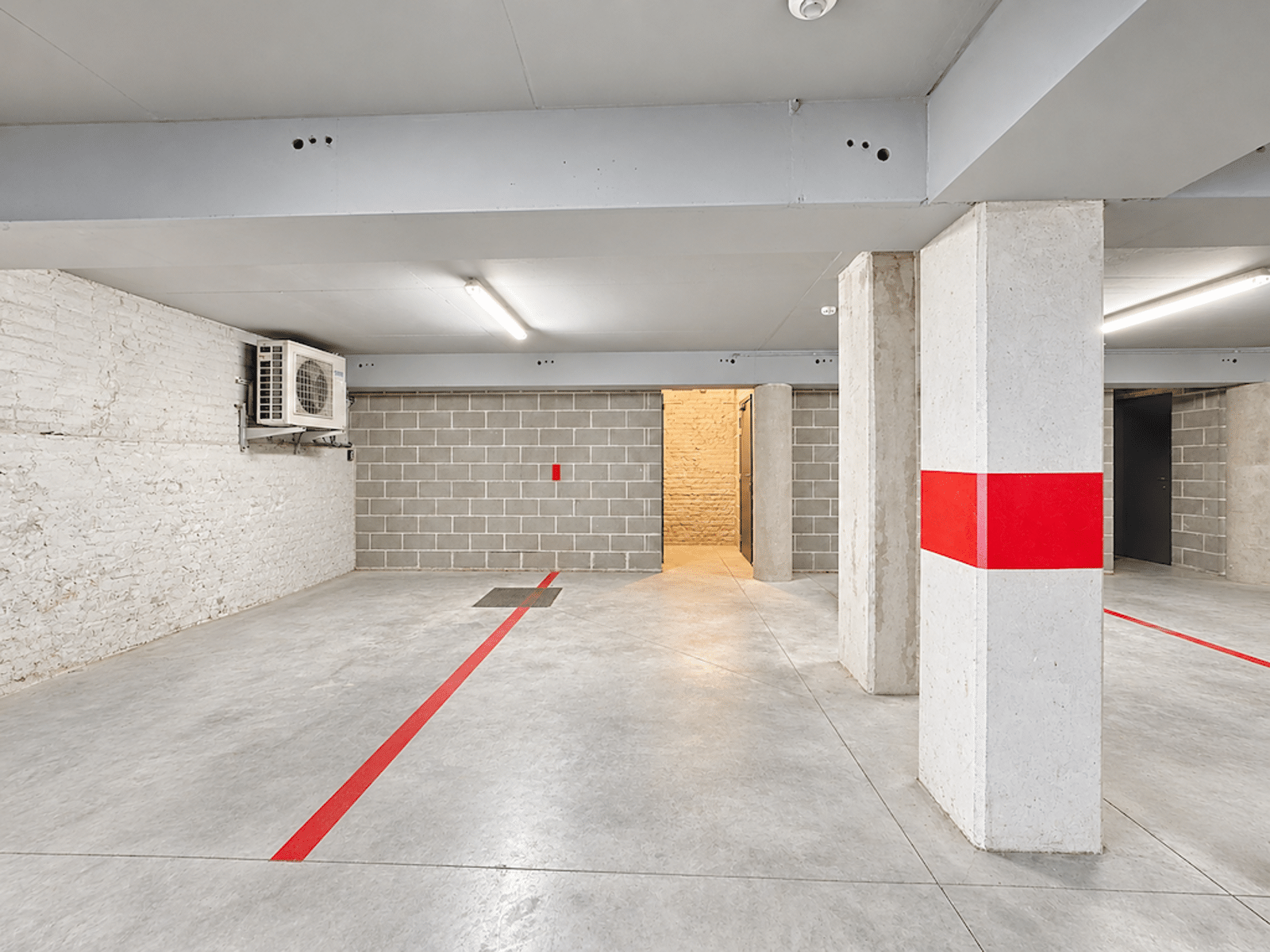 Parking Intérieur avec Marquages Rouges – You Real Estate Agency Parking intérieur sécurisé avec marquages rouges et colonnes en béton dans immeuble moderne.