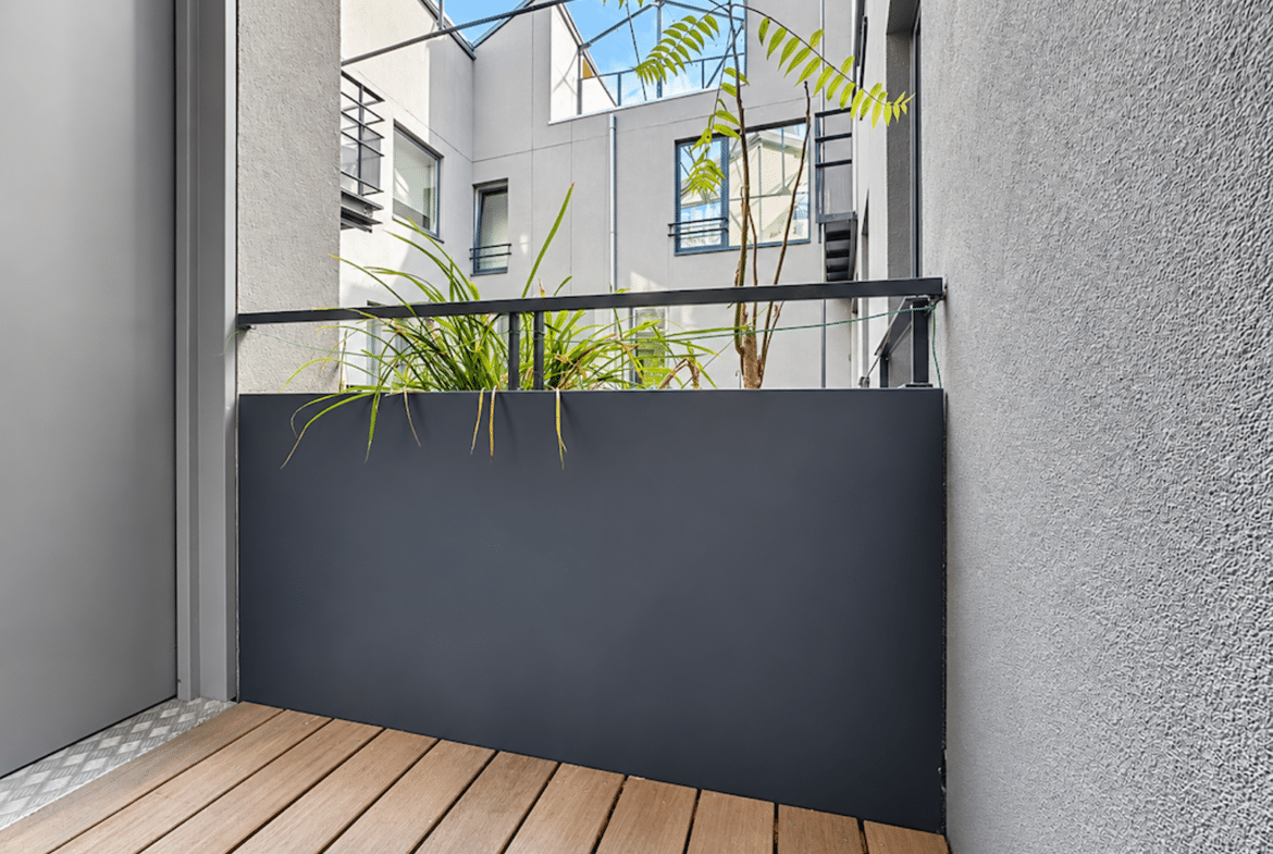 Terrasse en bois d’un appartement moderne avec jardinière et cour intérieure lumineuse.