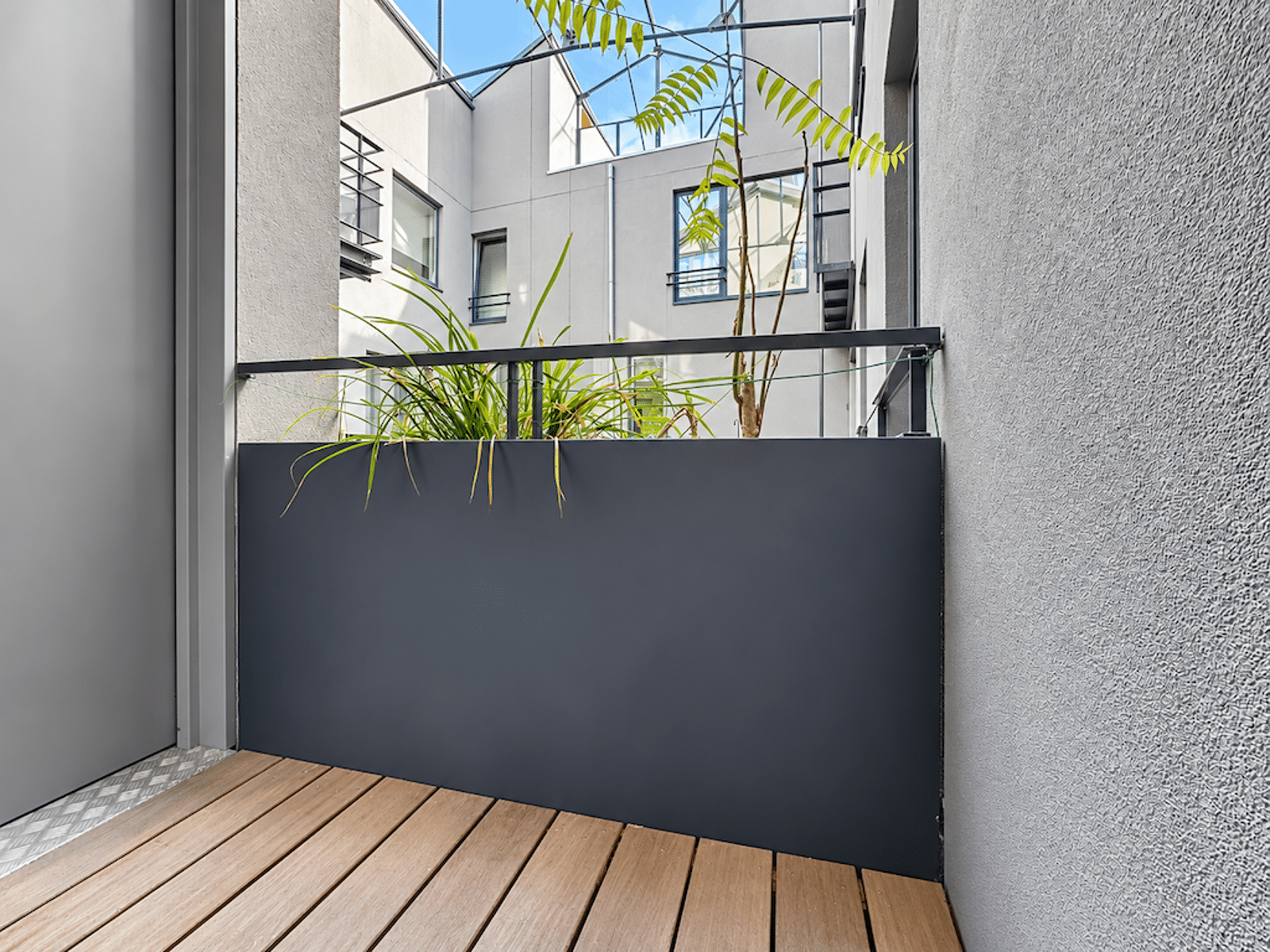 Terrasse en Bois avec Cour Intérieure – You Real Estate Agency Terrasse en bois d’un appartement moderne avec jardinière et cour intérieure lumineuse.