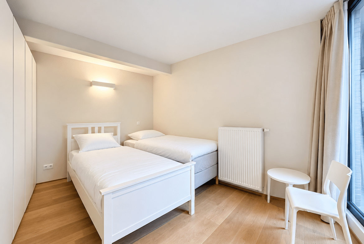 Chambre lumineuse avec deux lits simples et rangements intégrés dans appartement moderne.